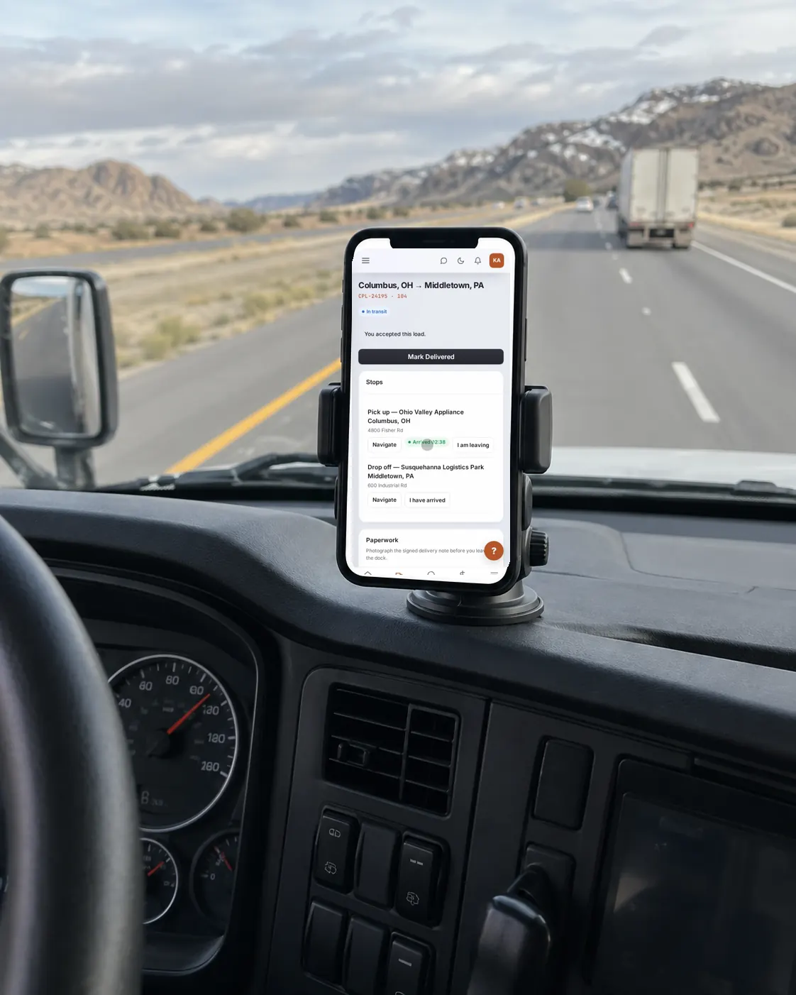 A phone on a truck’s dashboard showing the driver’s load: the stops, Navigate and Mark Delivered.